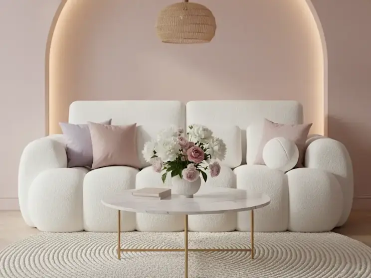 Kremowa sofa Cotonn w tkaninie Paolli 01 ustawiona w eleganckim salonie z dekoracyjną wnęką w kształcie łuku z podświetleniem, okrągłym stolikiem kawowym i bukietem kwiatów, tworząca jasną i harmonijną aranżację wnętrza.