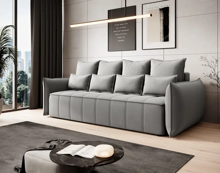 Nowoczesna kanapa Wellton w szarym kolorze z poduszkami oparciowymi, w eleganckim salonie z grafikami na ścianie i dywanem.