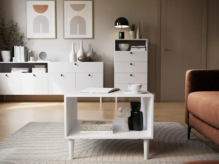 Nowoczesny salon z meblami Dullum: stolikiem kawowym, regałem i komodą w bieli, uzupełnionymi dekoracjami i naturalnym światłem.