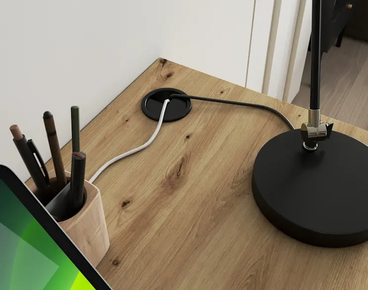 Drewniany blat biurka Barold w dekorze dębu z czarnym przepustem kablowym. Na blacie stoi czarna lampa, a obok kubek na długopisy i fragment monitora w aranżacji domowego biura.