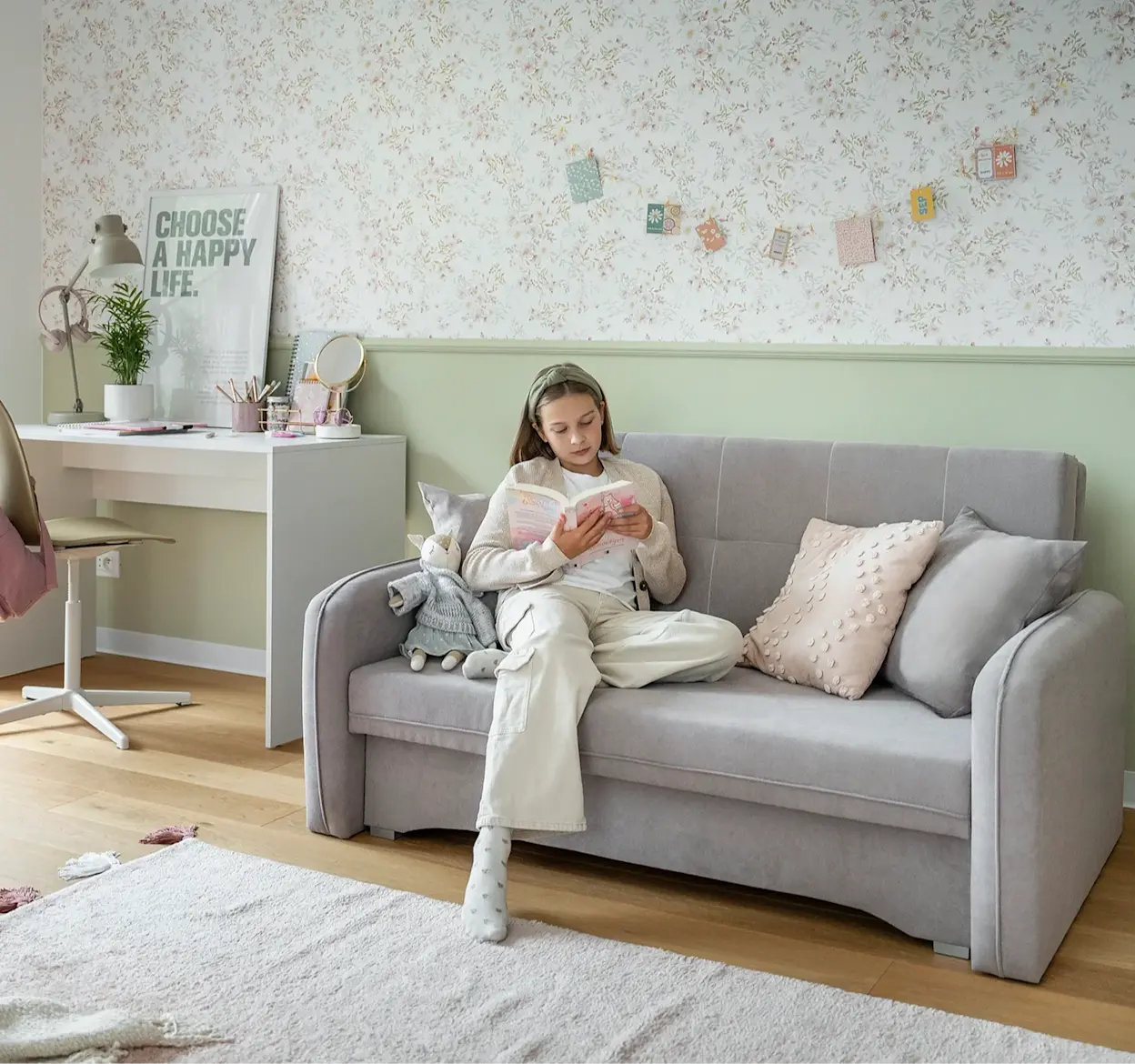 Kanapa Laine i biurko Nevy w przytulnym pokoju młodzieżowym, gdzie dziewczynka czyta książkę na sofie otoczonej pastelowymi dodatkami.