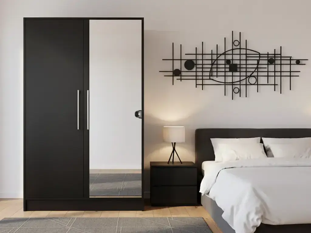 Szafa Alarica II w kolorze czarnym z lustrem ustawiona w stylowej sypialni z jasną pościelą, drewnianą podłogą i subtelnym oświetleniem. Kontrast kolorów oraz odbicie światła w lustrze tworzą harmonijną i nowoczesną przestrzeń.