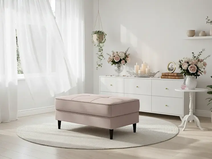 Elegancka pufa Bellis Gojo 101 w jasnym salonie, ustawiona na okrągłym dywanie, otoczona kwiatami i delikatnymi dekoracjami w kobiecym stylu.