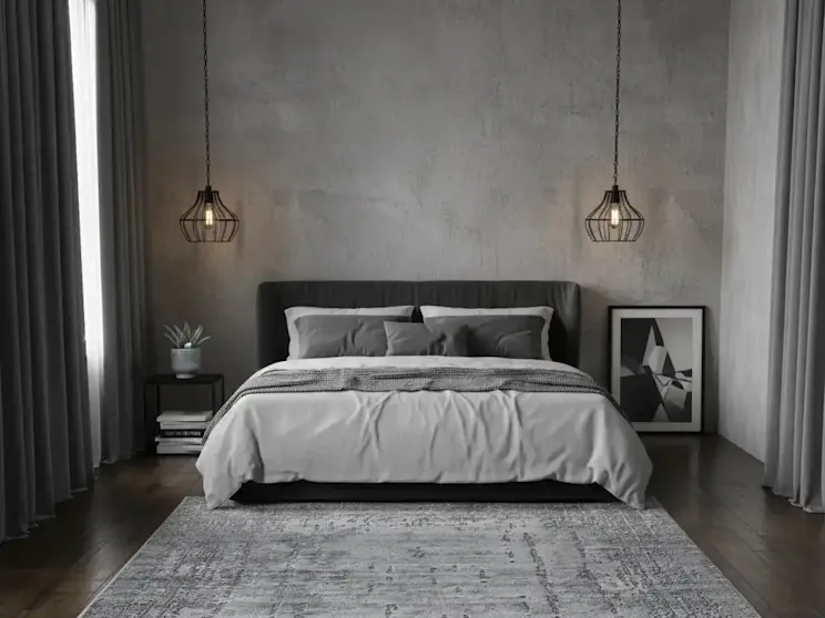 Dywan Codrila Grey w nowoczesnej sypialni w stylu loftowym, ułożony na ciemnej drewnianej podłodze przed łóżkiem z szarym zagłówkiem. Subtelny wzór dywanu i stonowana kolorystyka idealnie pasują do industrialnych ścian i minimalistycznych dodatków.
