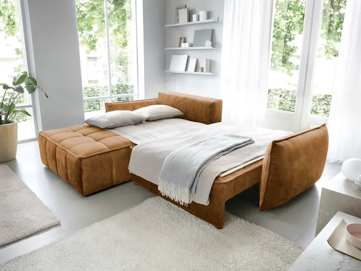 Narożnik Campo w funkcji spania, z miękką pościelą i kocem, ustawiony w jasnym wnętrzu z naturalnym światłem i minimalistycznymi dodatkami.