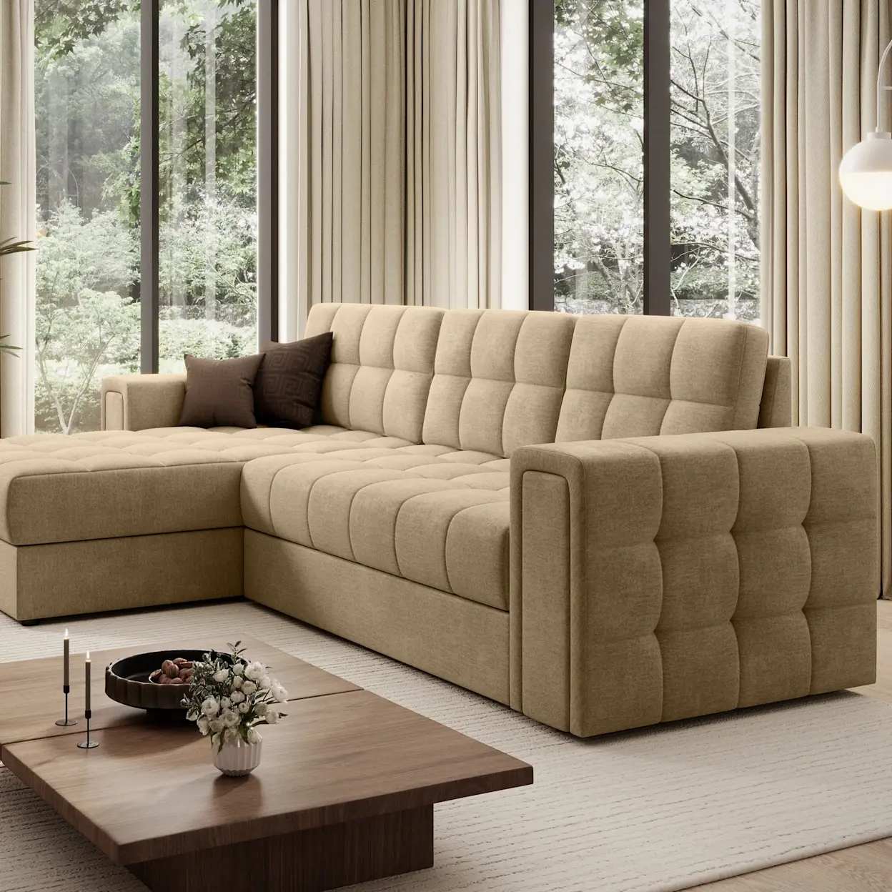 Inspiracja salonu z beżowym narożnikiem Blenvi Monolith 09 o pikowanym siedzisku i szerokich podłokietnikach. W tle duże przeszklenia z widokiem na zieleń, jasne zasłony oraz niski stolik kawowy z dekoracjami.