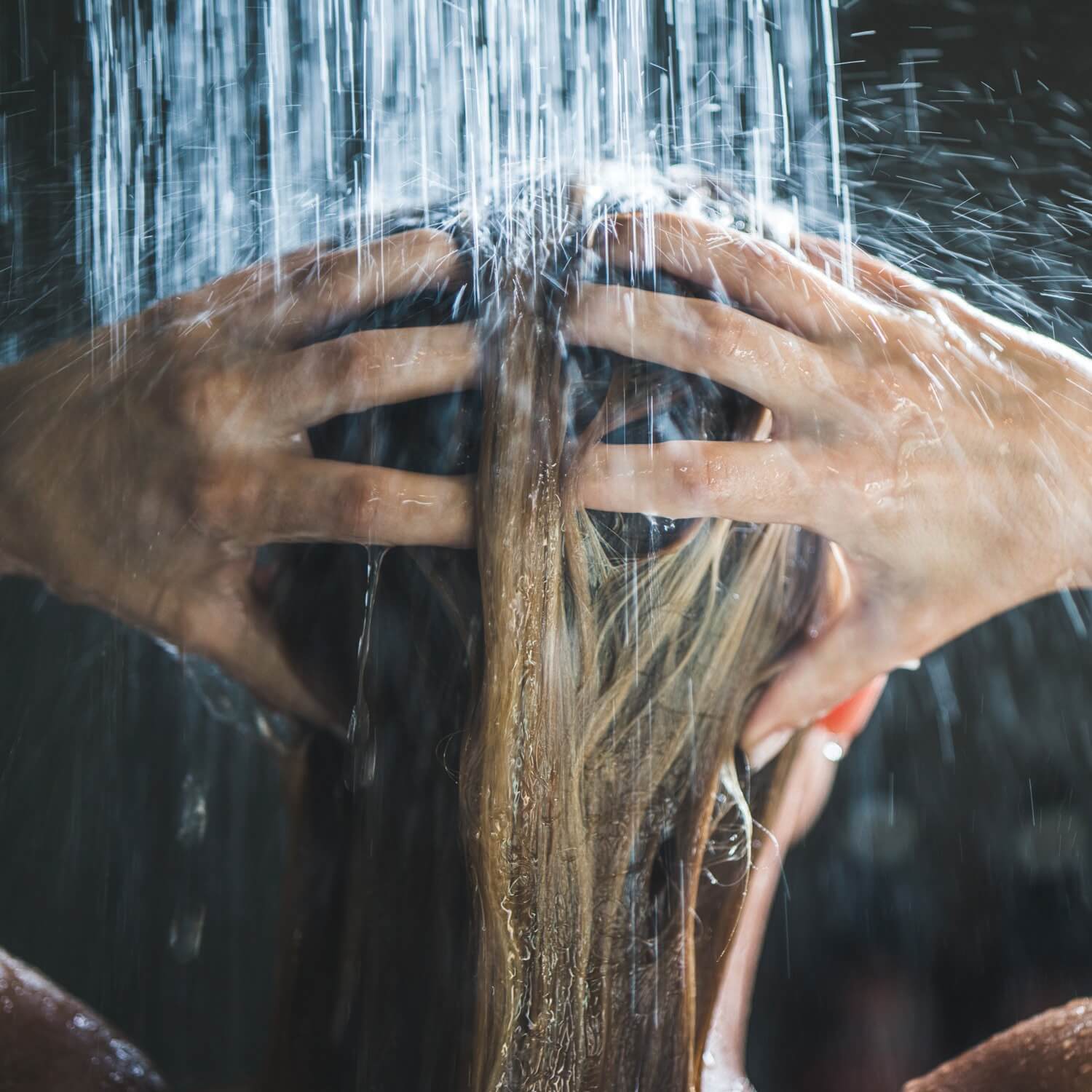 Mulher toma banho de costas lavando o cabelo.
