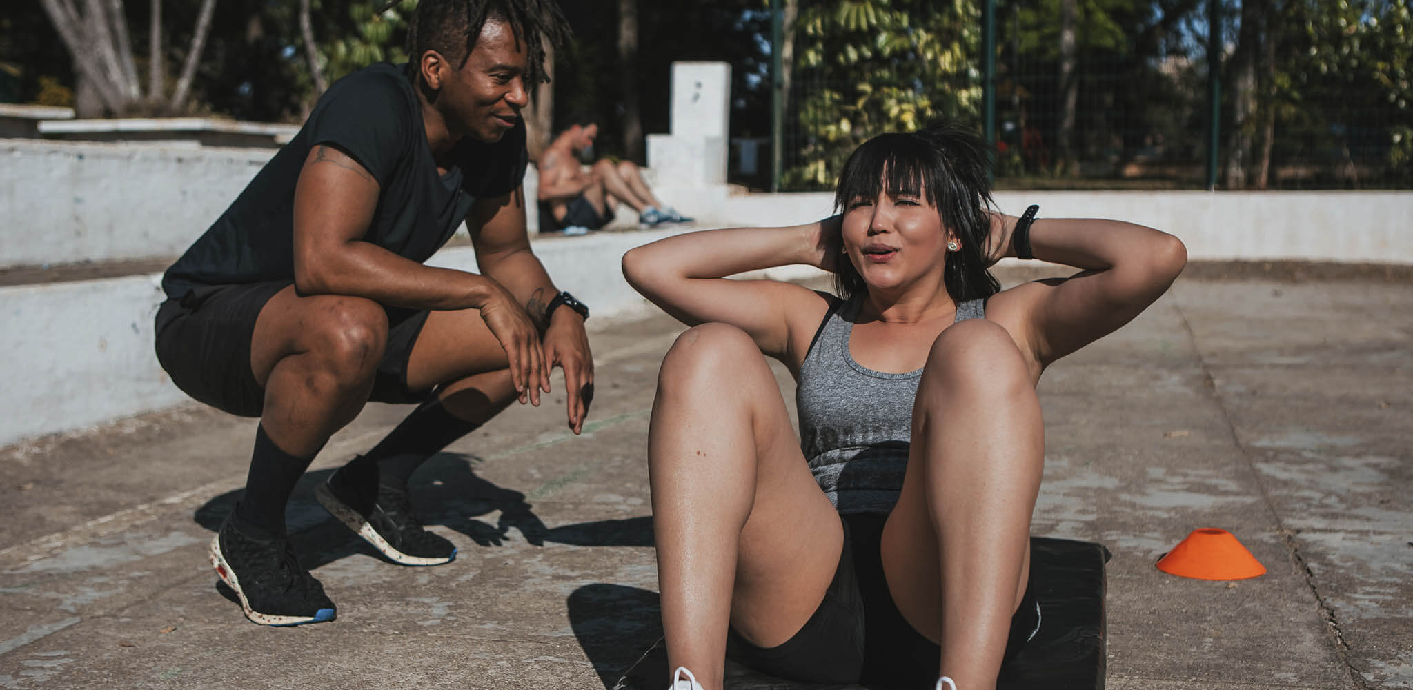 Mulher faz exercício abdominal enquanto interage com amigo 