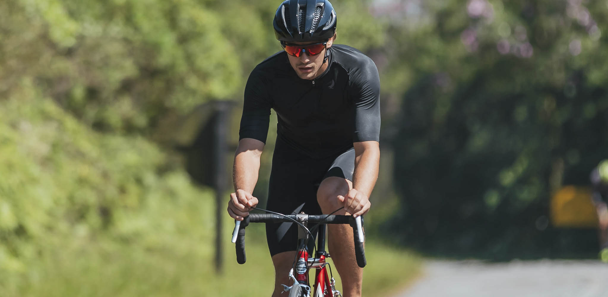 Homem pedala em rodovia, com área verde ao redor