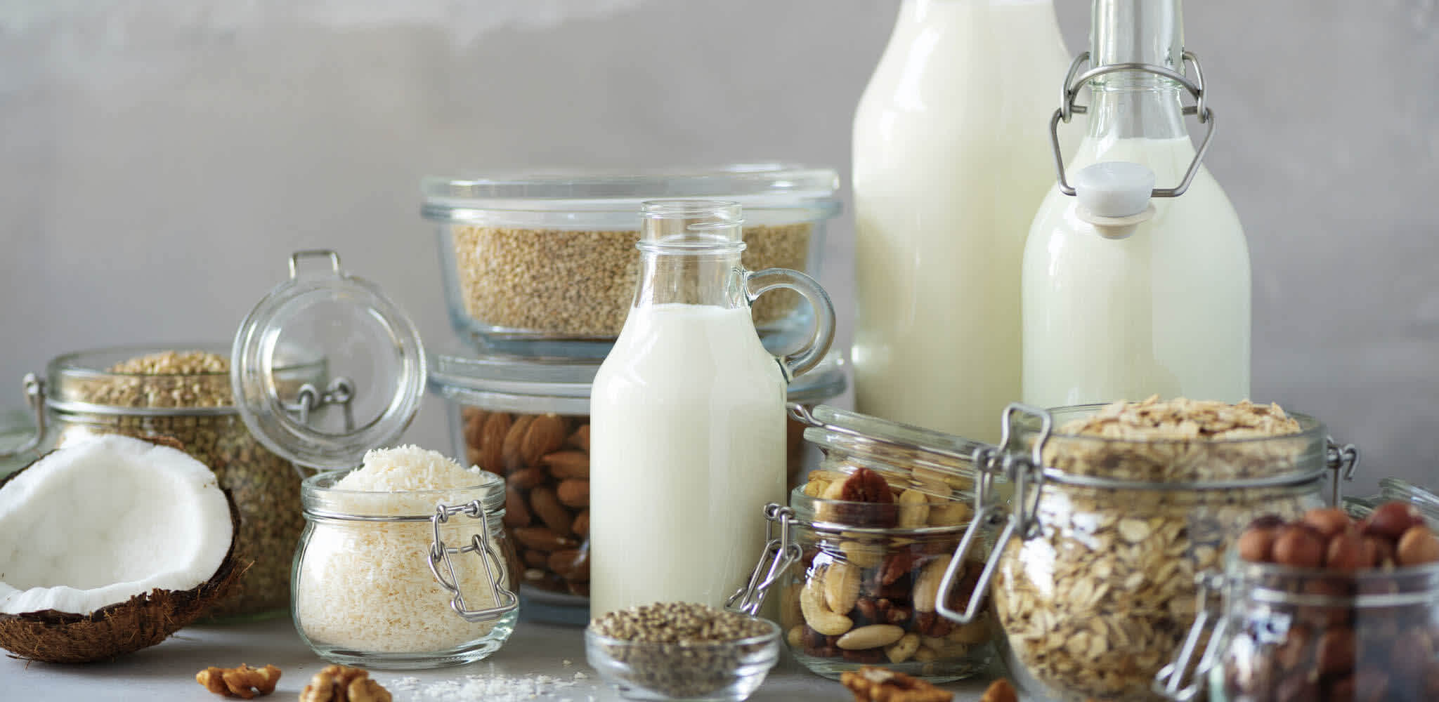 Garrafas de leite de tamanhos variados e potes de cereais como granola e aveia expostos sobre uma mesa