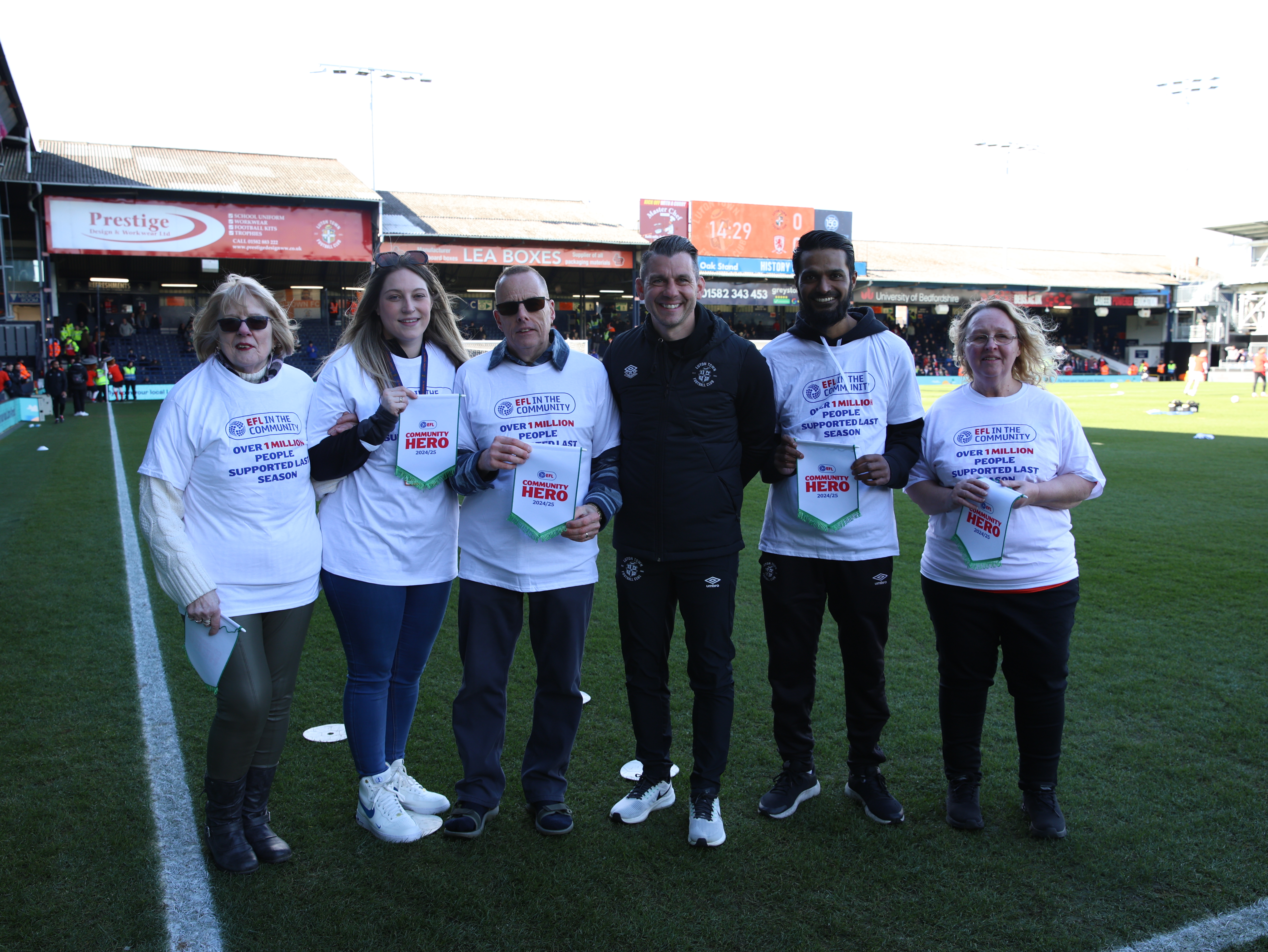Manager Matt Bloomfield presents EFL Community Hero pennants to Pauline Blanchard, Beth Drake, Martin Quigley, Shipaar Miah and Sue Waddacor on the Kenilworth Road pitch before the game against Middlesbrough.