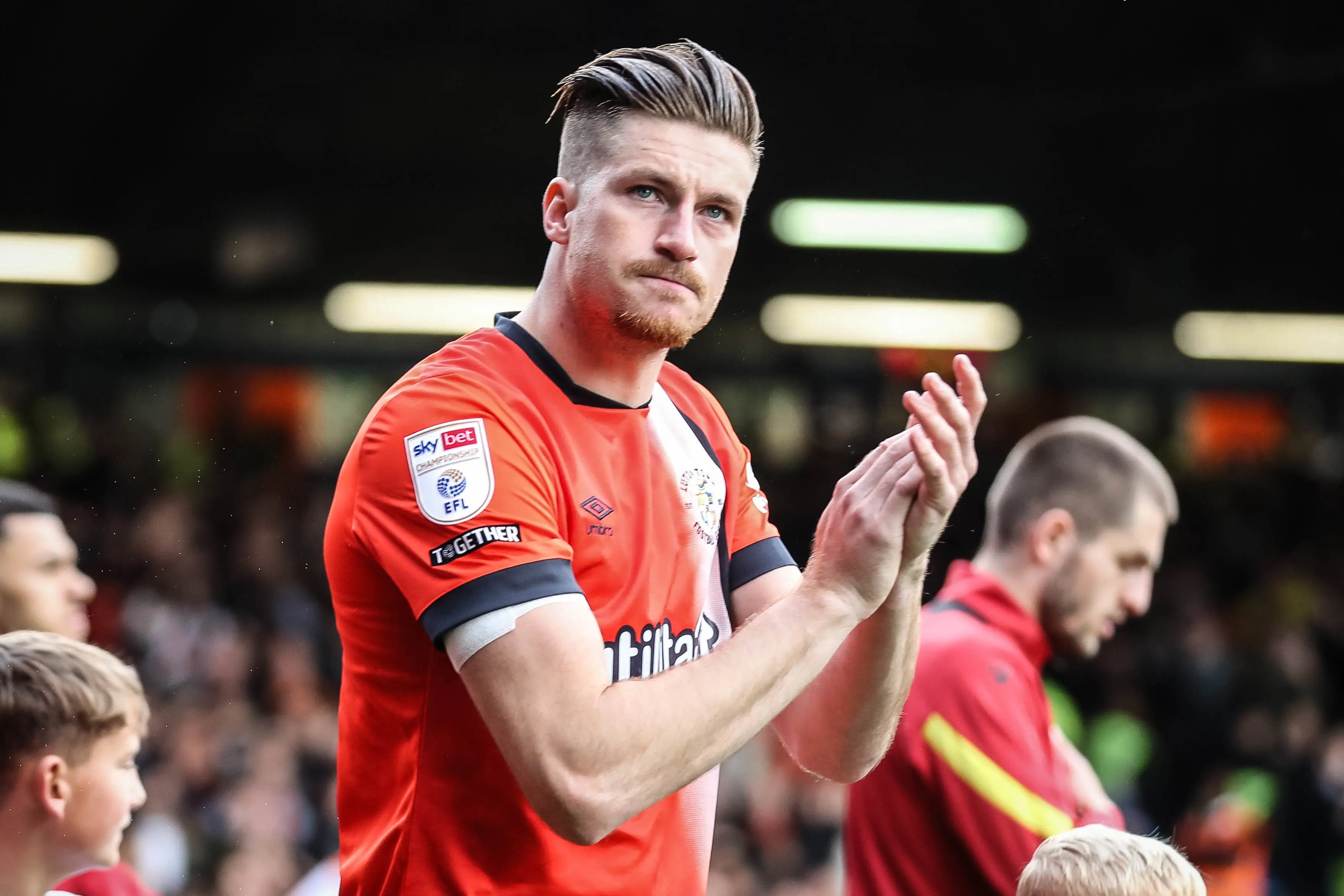 Reece Burke applauds the crowd as he comes onto the pitch at Kenilworth Road before a game.