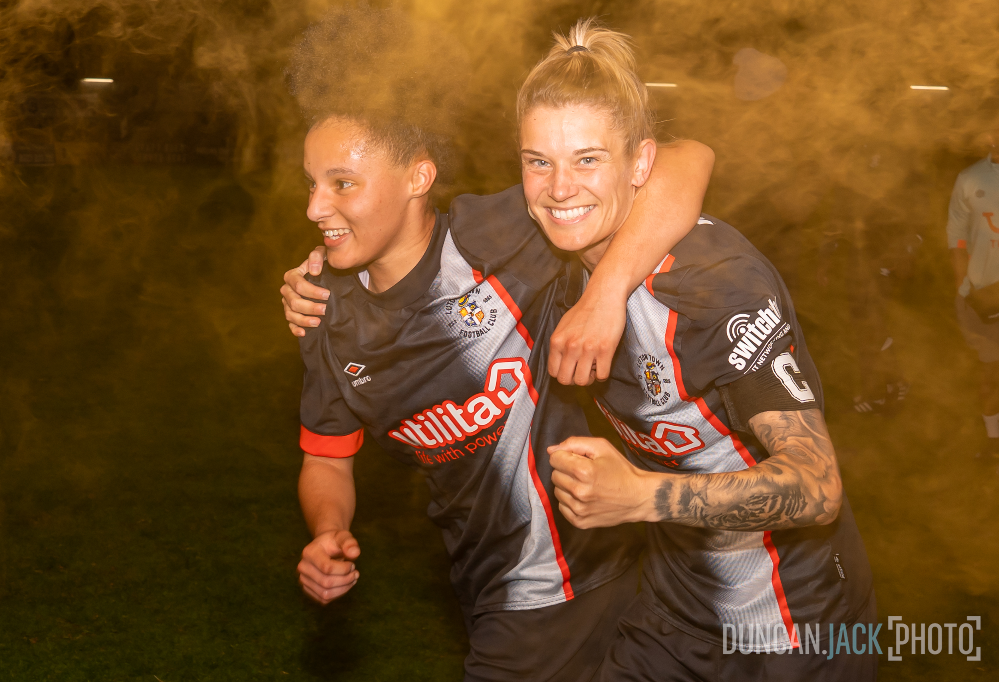 Shanice Lewis and Elly Wade celebrating at St Albans, with an orange flare in the background and foreground.