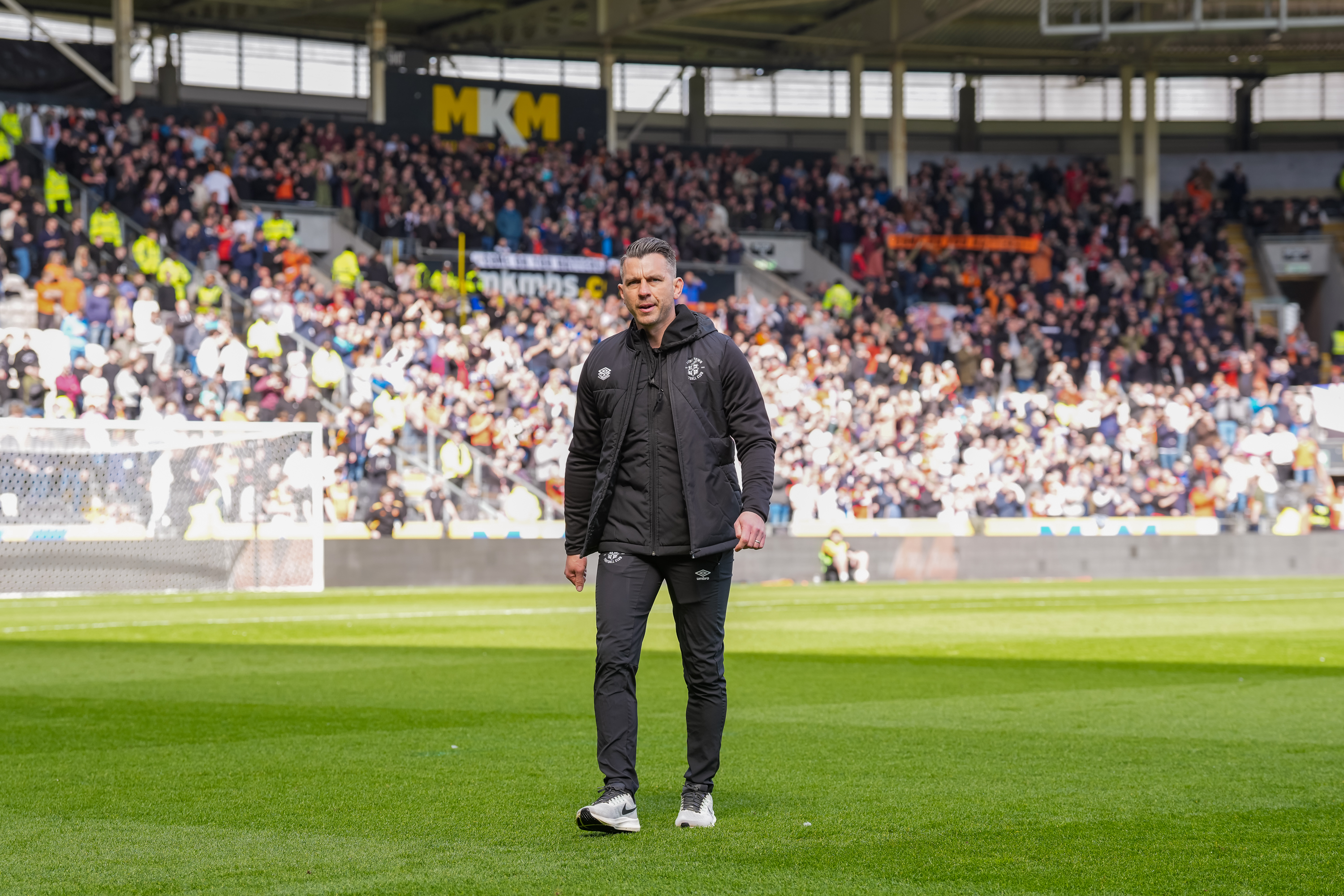 Matt Bloomfield walks off the pitch at the MKM Stadium with Luton Town supporters in the background.