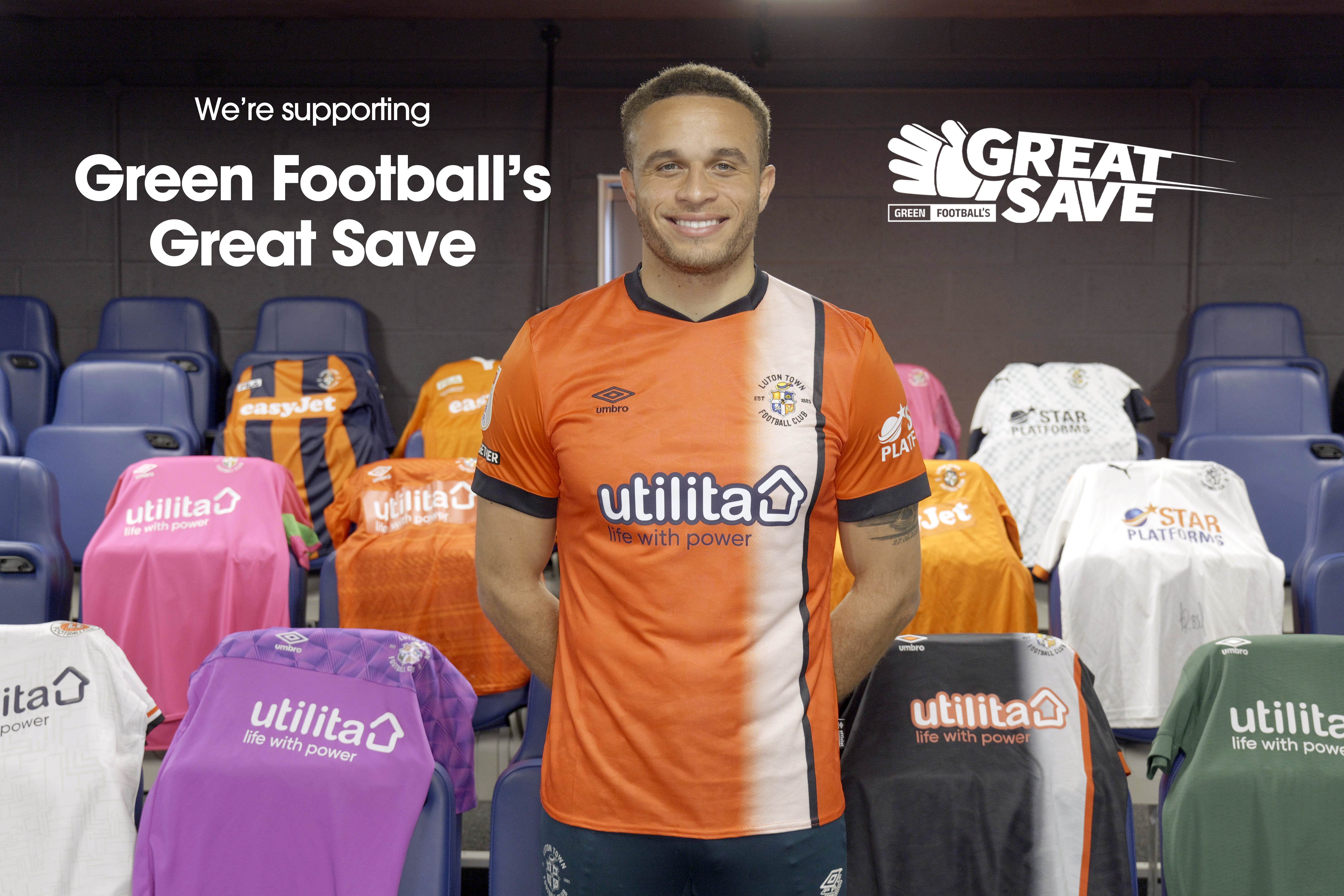 Hatters captain Carlton Morris wearing his home shirt with a collection of Luton Town home, away and goalkeeper shirts around him to promote Green Football's Great Save campaign, recycling old kits.