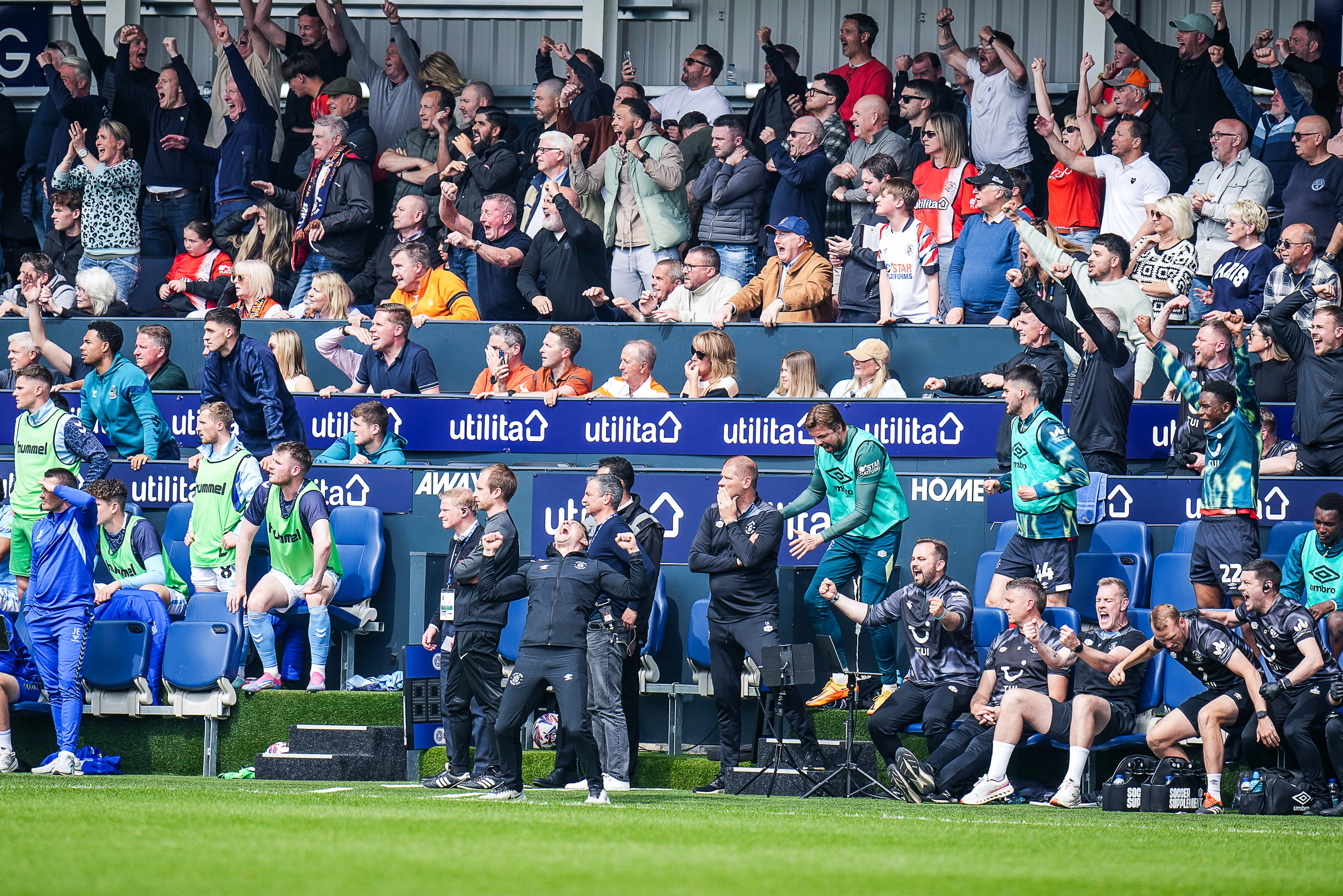 Supporters in the Dug Out hospitality package seats celebrate a Hatters goal with manager Matt Bloomfield, his staff and the Town bench right in front of them.