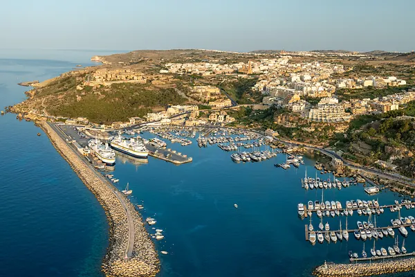 Aerial view of Mgarr Harbour where yachts bob gently in the turquoise water, overlooked by the town's sandstone buildings, Gozo, Malta.