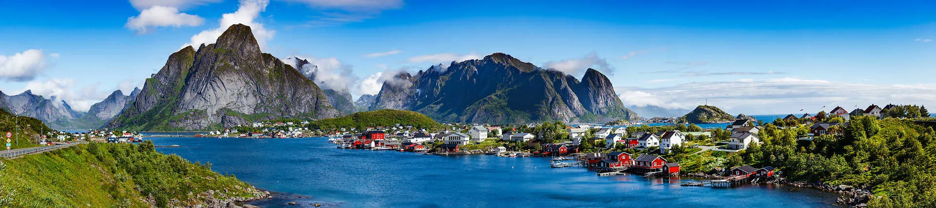 Panorama der Lofoten in Norwegen mit steilen Bergen und Fischerhütten am Meer.
