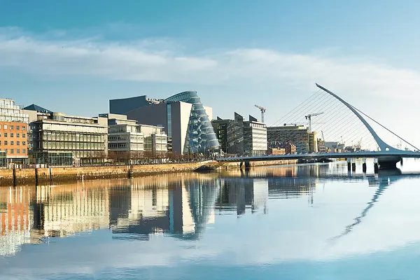 Modern buildings and offices on Liffey river in Dublin on a bright sunny day, bridge on the right is a famous Harp bridge.