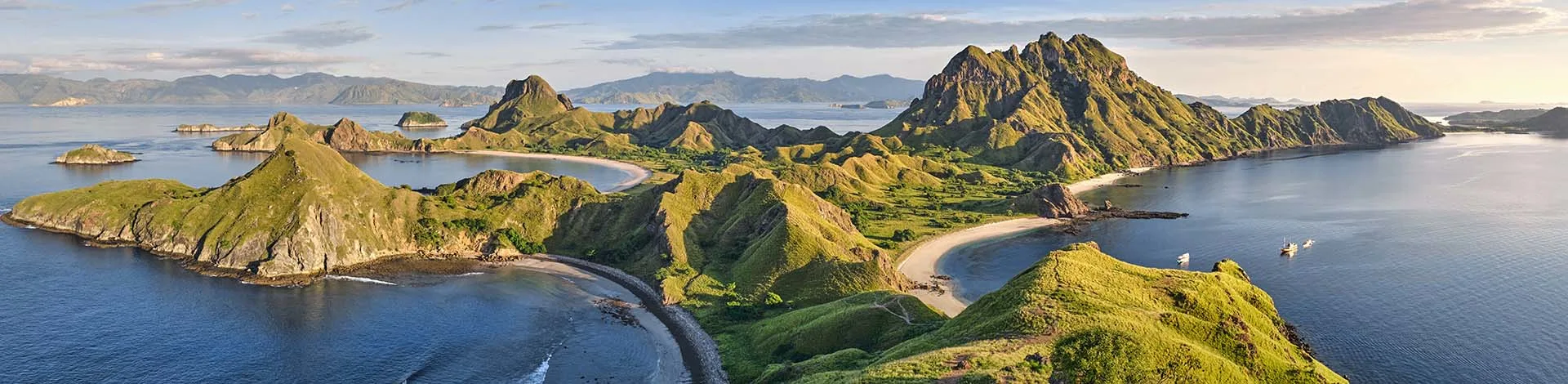 A panoramic view of Padar Island in Komodo National Park, with its striking green hills, sweeping sandy beaches, and the surrounding blue sea in daylight.