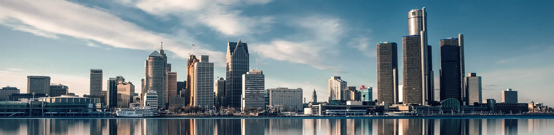 Panoramasicht auf die Skyline von Detroit, Michigan mit dem Renaissance Center und weiteren Wolkenkratzern, die sich im ruhigen Wasser des Detroit River widerspiegeln.