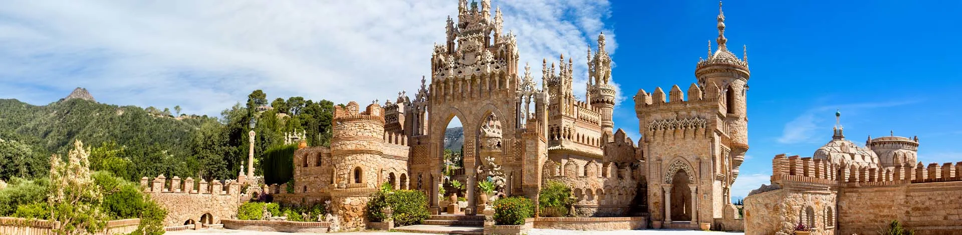 Panoramaaufnahme des Castillo de Colomares in Benalmádena bei Málaga, einer kunstvollen schlossartigen Anlage mit detailreichen Türmen und Bögen vor blauem Himmel.