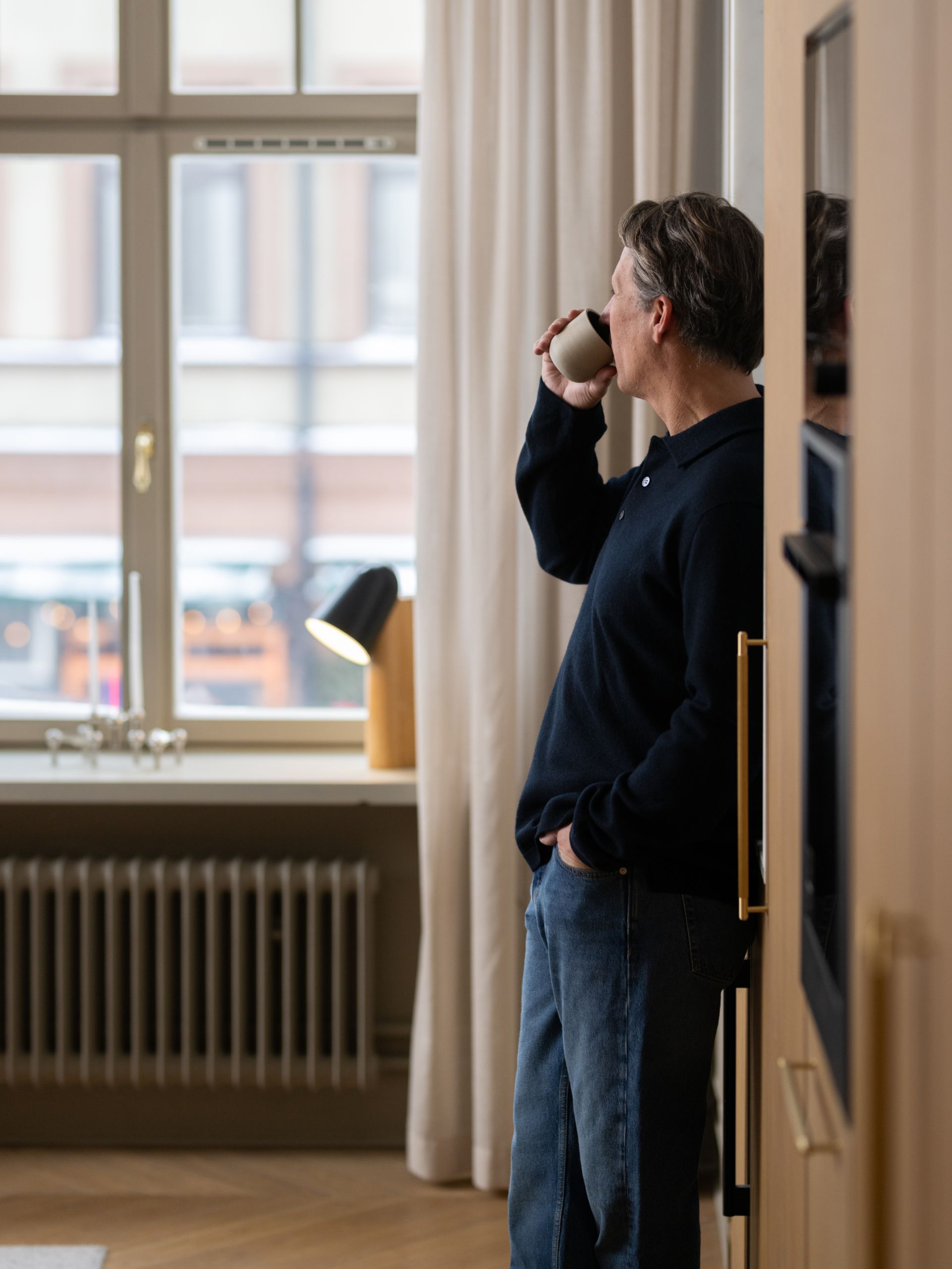 Man står vid ett fönster och dricker kaffe, med blicken riktad ut mot gatan utanför.