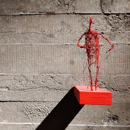 Mensfiguur gemaakt van rood touw op een rood plankje.