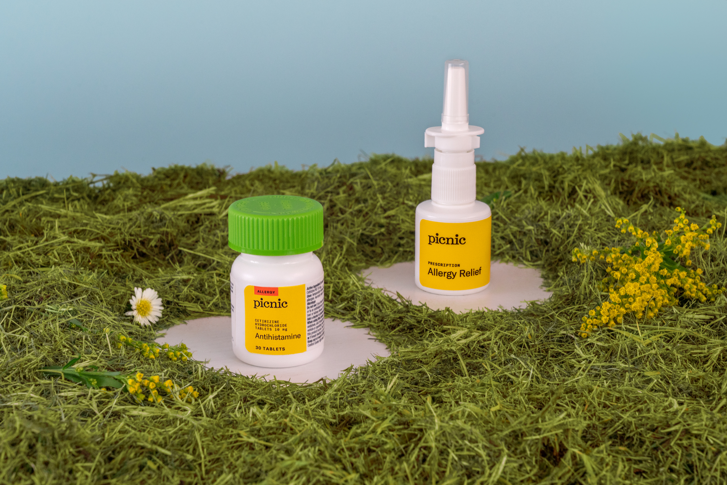 Photo of two bottles of Picnic allergy treatment surrounded by grass and flowers.