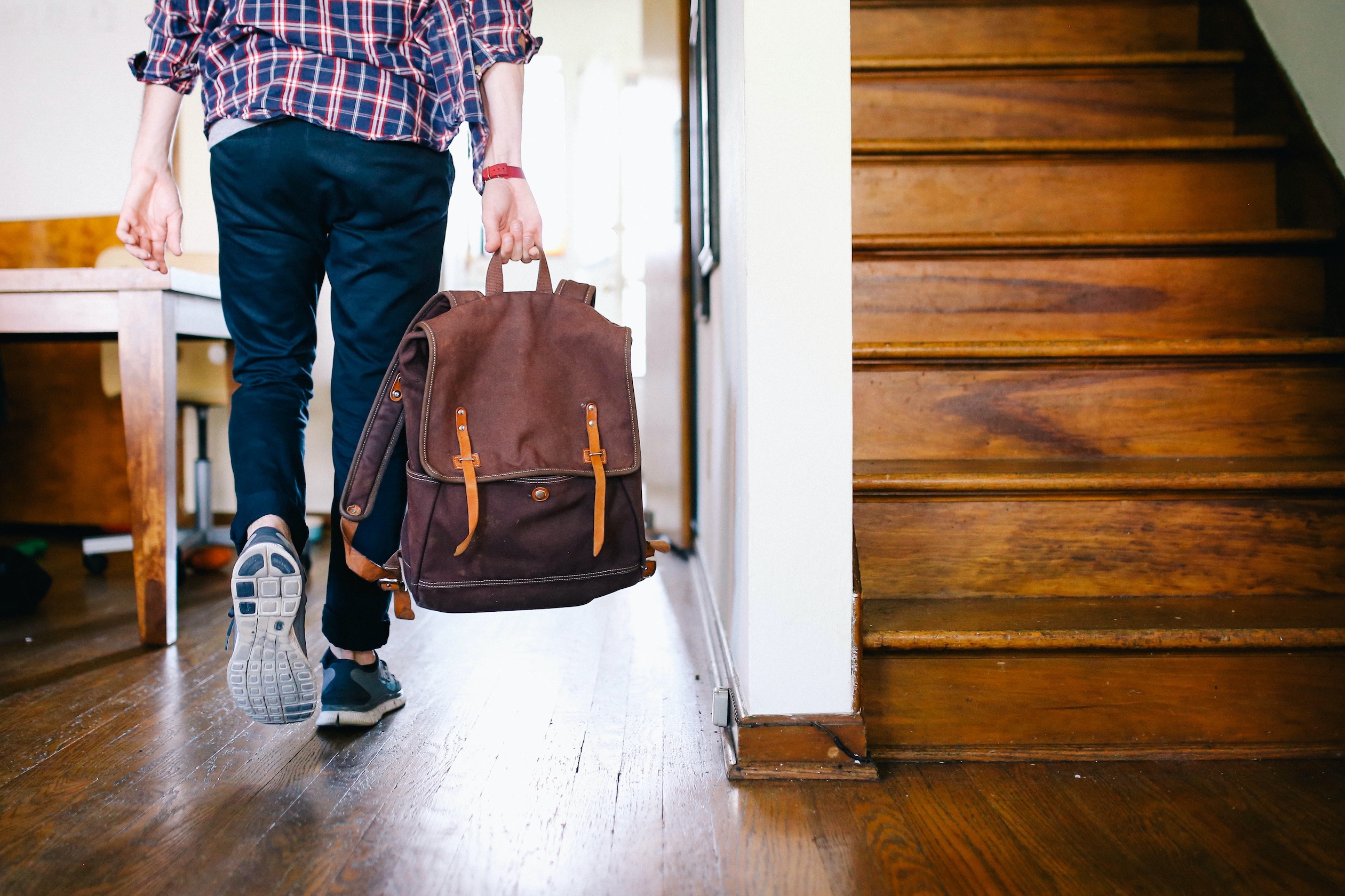 Photo of a person walking through their home wearing sneakers and carrying a backpack.