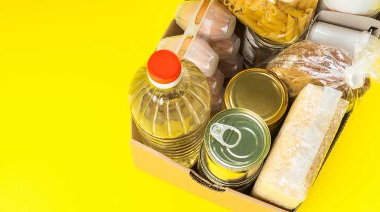 Box of pantry items, eggs, oil, and pasta on yellow background