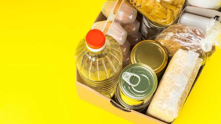 Box of pantry items, eggs, oil, and pasta on yellow background