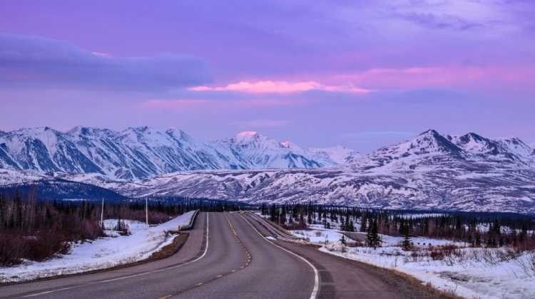 open road in Alaska, with snow-covered mountains in twilight