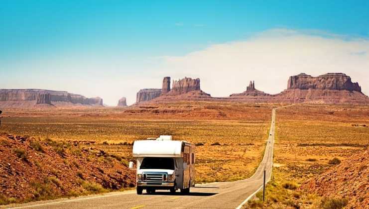 photo of RV driving on road with red rock formations behind it