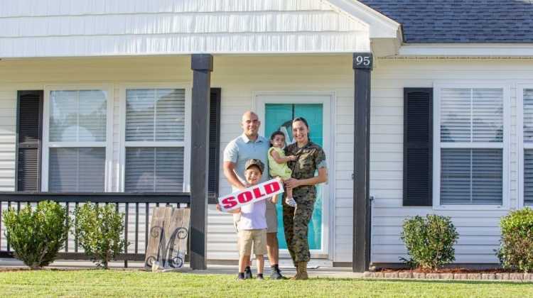 marine family holding a sold sign in front of house