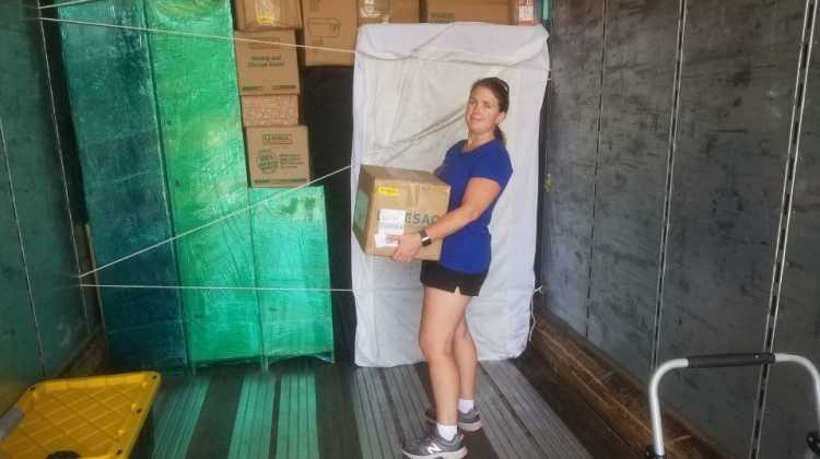 Woman holding cardboard box inside moving truck, with stacks of boxes behind her