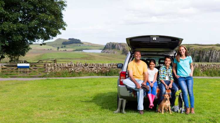 Family in front of car during a cross-country road trip with kids and visit to a national park site