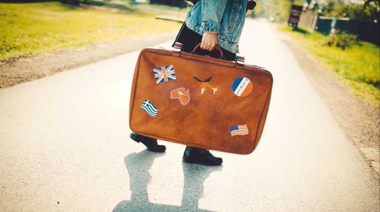 person holding suitcase with travel stickers