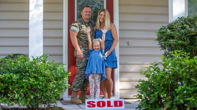 Marine family standing behind sold sign