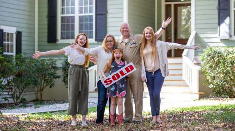 military family holding sold sign in front of home