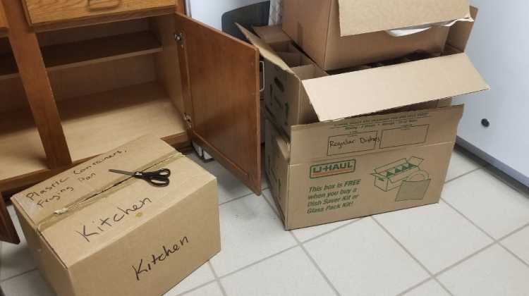 image of empty kitchen cabinets and carboard moving boxes labeled "Kitchen"