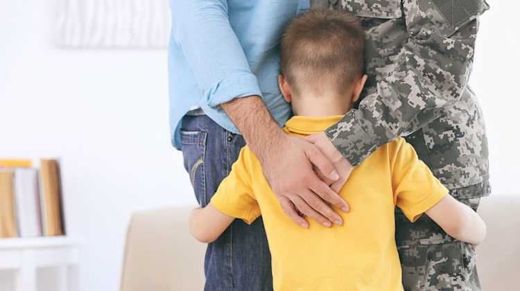 Back view of child being hugged by two parents, one in the military