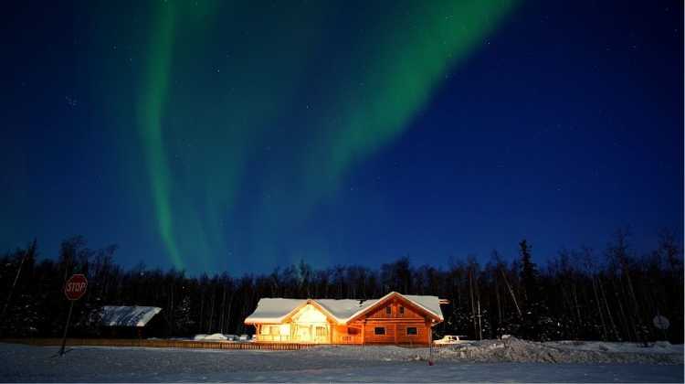 Night photo of a log cabin in the snow with the Northern Lights in the sky