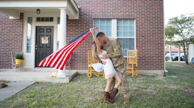 Military couple in front of a new home with an American flag are happy and finding joy at their new duty station