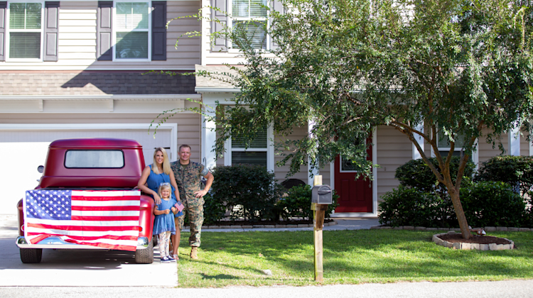 military couple leaning on truck with home in the background