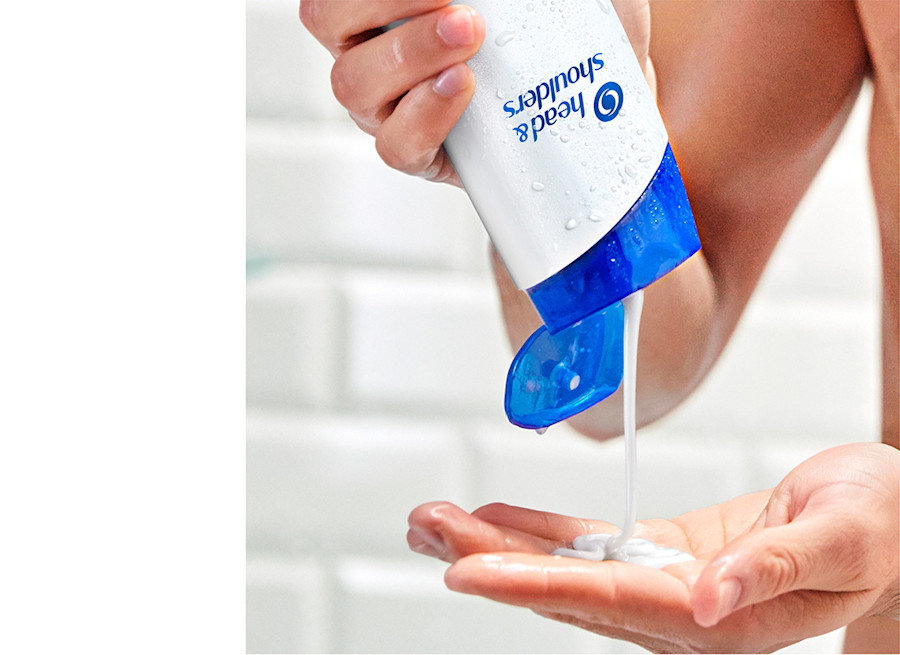 Shampooflasche von Head & Shoulders wird kopfüber in der Hand gehalten, Shampoo wird auf die Hand gedrückt.