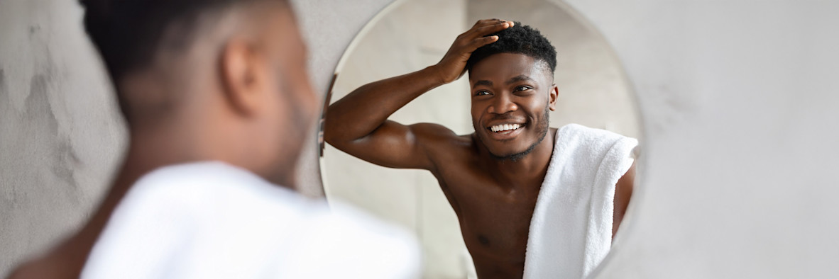 Ein Mann berührt mit besorgtem Ausdruck seine Kopfhaut vor einem Spiegel.