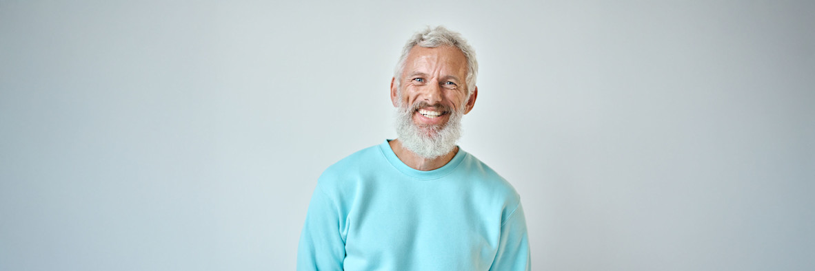 Ein älterer Mann mit kurzen grauen Haaren lächelt herzlich und trägt ein türkisfarbenes Oberteil.