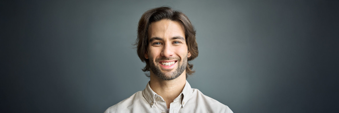 Ein lächelnder Mann mit langem, gesund aussehendem dunklem Haar trägt ein weißes Hemd.