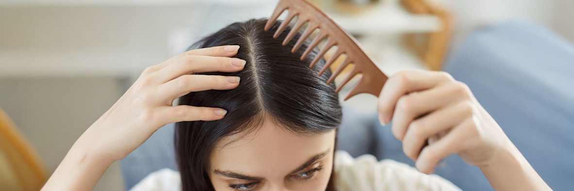 Eine Frau verwendet einen Kamm mit feinen Zähnen, um ihr dunkles Haar zu scheiteln und durchzukämmen.